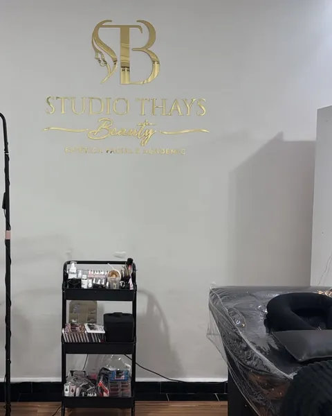Luminária em meia-lua sobre a maca, com o logotipo dourado do studio na parede ao fundo.