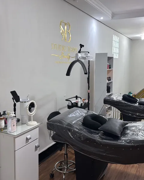 Sala de atendimento com macas pretas, carrinho de apoio e o logotipo dourado do studio na parede.