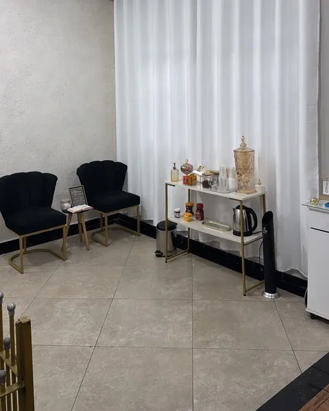 Recepção do studio com duas poltronas pretas de pés dourados, mesa de café e cortinas brancas.