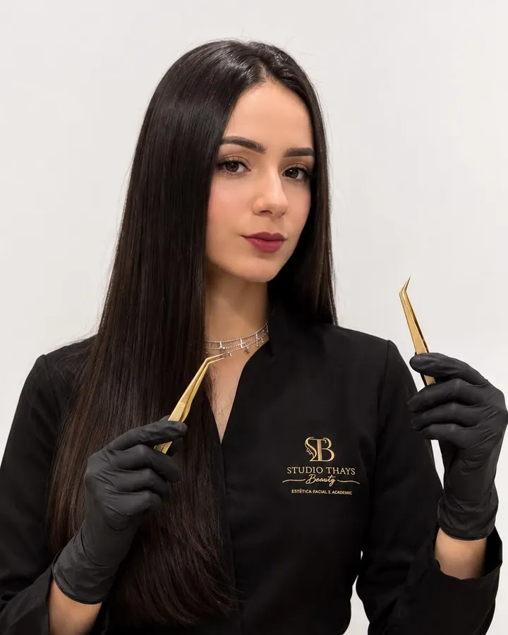 Thays, de uniforme preto com o logotipo do studio, segurando duas pinças douradas.